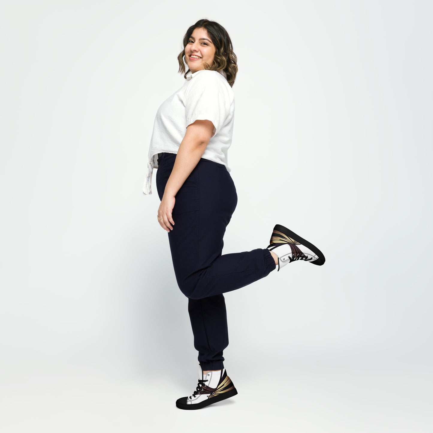 Woman lifting leg in the air, wearing black Aylure Eirith high top sneakers with unique design and black laces